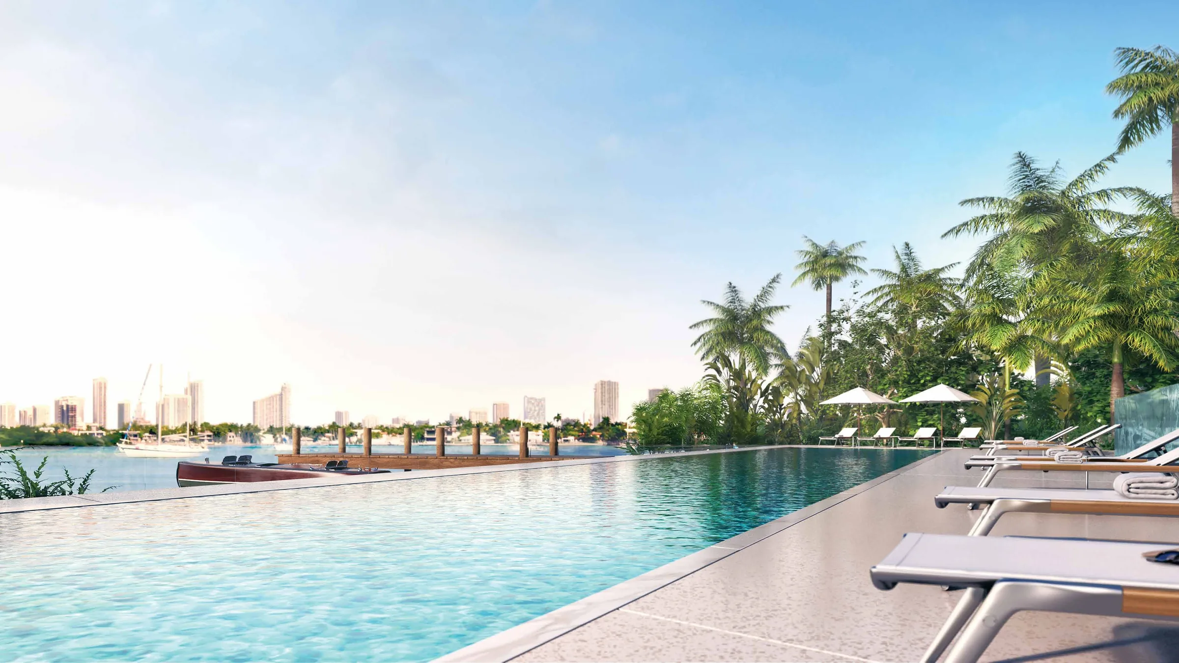 The 116-foot pool along the bay edge, loungers and palms beside the water with the dock and skyline beyond